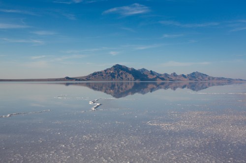 A serene landscape featuring a salt flat reflecting mountains under a clear blue sky.