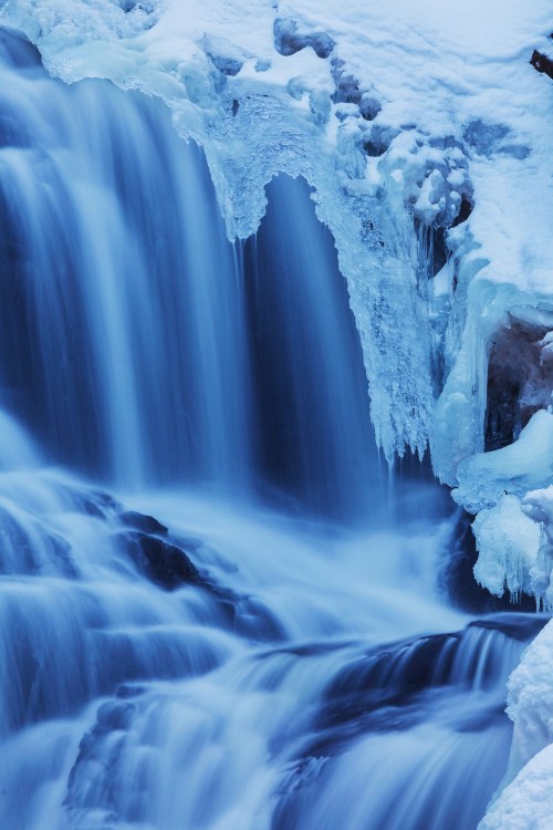 A serene waterfall cascading over icy rocks, surrounded by frozen icicles and a soft blue hue.