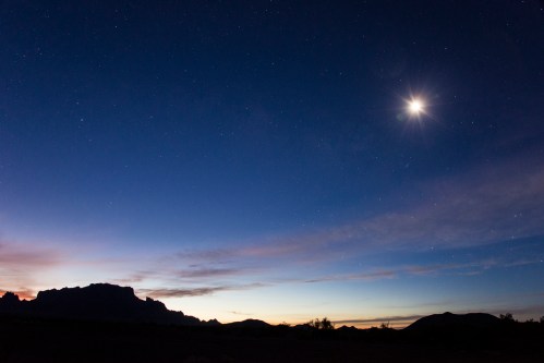 A twilight sky with stars and a bright crescent moon above a silhouetted mountain range.