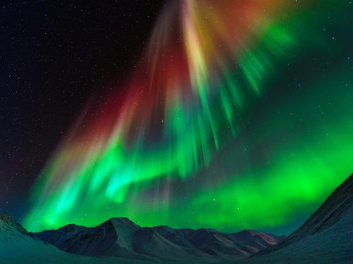 Vibrant auroras dance across a starry night sky, illuminating snow-capped mountains in shades of green, red, and purple.