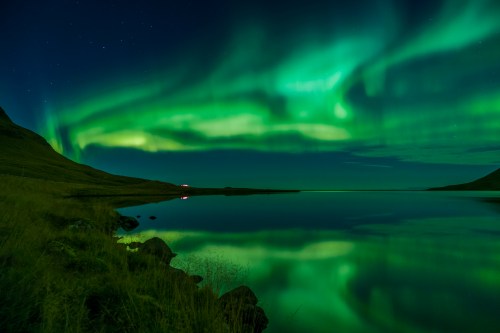 A serene landscape featuring a lake reflecting vibrant green auroras under a starry night sky.