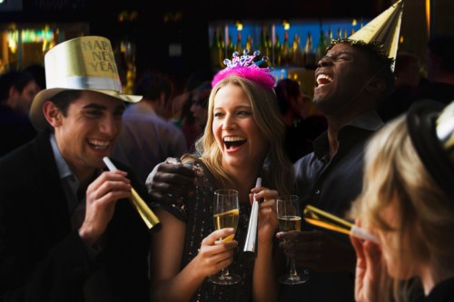 A group of friends celebrating New Year's Eve, wearing party hats and holding drinks, laughing and enjoying the moment.