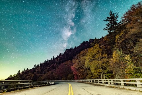A winding road under a starry sky, with colorful autumn trees lining the mountainside.