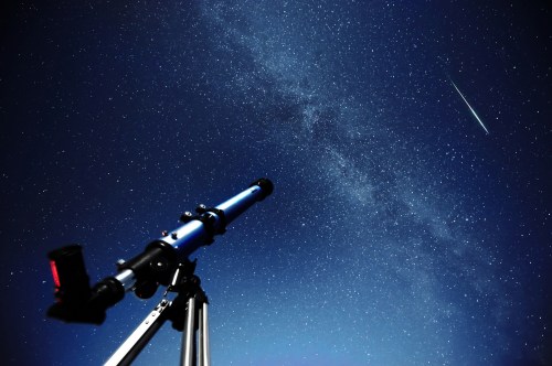 A telescope points towards a starry night sky with a bright meteor streaking across the scene.