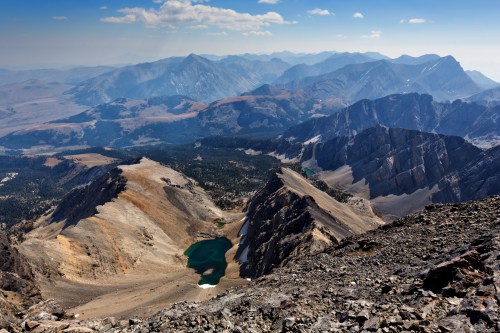 A panoramic view of rugged mountains and a serene lake nestled in a valley under a clear blue sky.