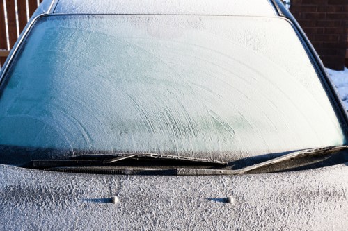 Frost-covered windshield of a car, with visible ice patterns and a snowy background.