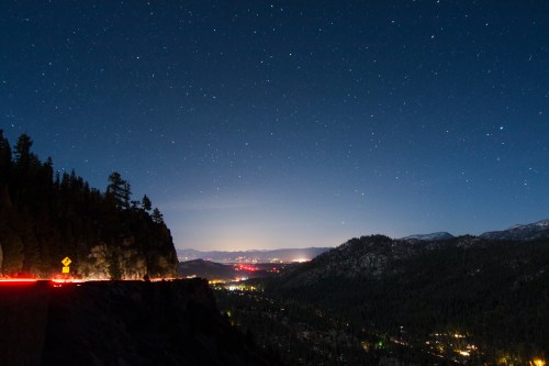 A starry night sky over a mountainous landscape, with city lights visible in the valley below.