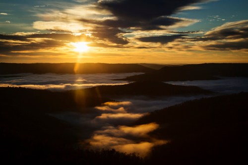 A stunning sunrise over misty valleys, with golden light breaking through clouds and illuminating the landscape.