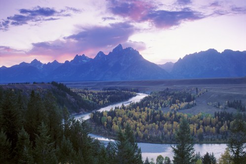 A serene landscape featuring a winding river, vibrant autumn trees, and majestic mountains under a colorful sky.
