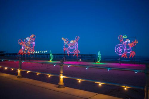 Colorful crab-shaped light displays on a beach at dusk, with a pier in the background and festive lights along the walkway.