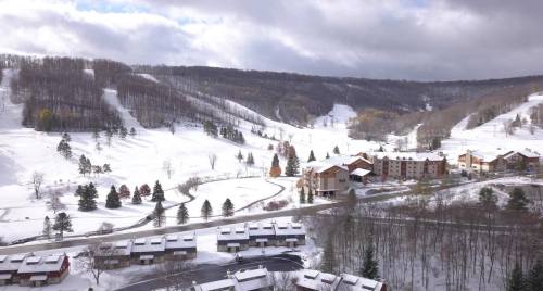 A snowy landscape with hills, trees, and a cluster of buildings in a winter resort setting.