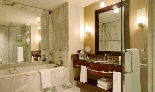 Modern bathroom featuring a marble design, a bathtub, a sink with a mirror, and soft lighting.