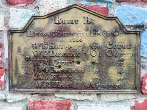 Bronze plaque on a stone wall, listing builders and officials from 1914, including names and titles.
