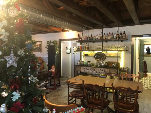 Cozy restaurant interior with wooden tables, a bar, and a decorated Christmas tree in the foreground.