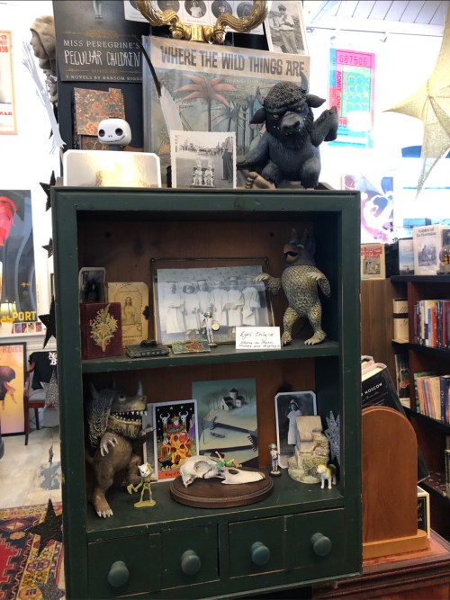 A vintage display cabinet filled with figurines, photos, and books, featuring whimsical creatures and nostalgic decor.