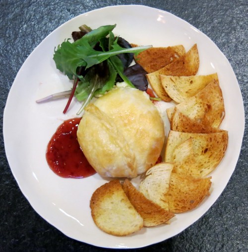 A plate with baked cheese, a side salad, and crispy bread slices, accompanied by a small serving of red sauce.