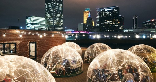 A rooftop scene featuring illuminated igloo-like structures with a city skyline in the background at night.