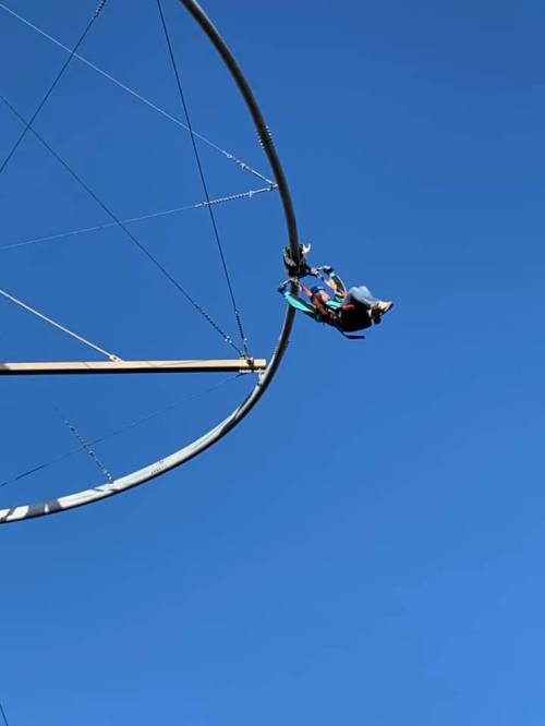 A person swings high on a circular ride against a clear blue sky.