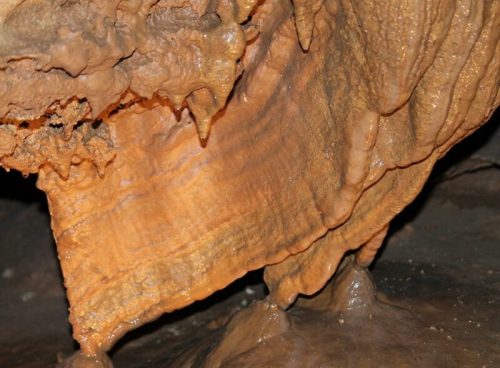 Close-up of a textured cave formation with orange and brown hues, showcasing stalactites and stalagmites.