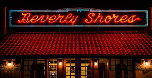 Neon sign reading "Beverly Shores" illuminated above a building with a tiled roof at night.