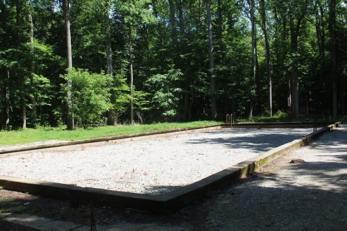 A gravel area surrounded by trees, likely an old swimming pool or recreational space, now empty and overgrown.