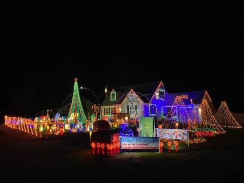 A brightly lit house decorated with colorful Christmas lights, featuring trees, figures, and festive displays at night.