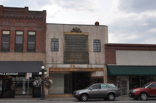 Historic building with a decorative facade, large windows, and a crown motif, set in a small town street.