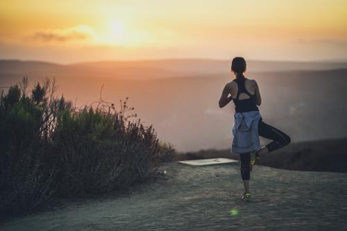 A woman practices yoga at sunset on a scenic overlook, surrounded by nature and mountains in the background.
