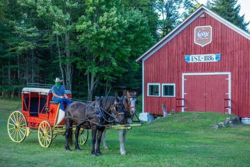 A horse-drawn carriage is parked in front of a red barn with "Est. 1886" sign, surrounded by trees.