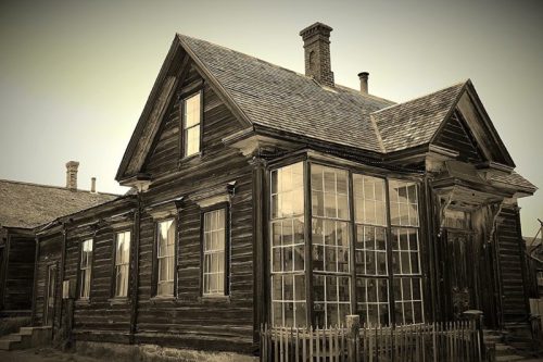 A vintage wooden house with a glass-enclosed porch, featuring a steep roof and a rustic fence.