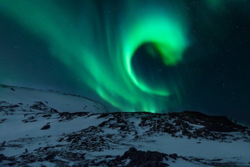 A stunning display of the northern lights swirling over a snowy landscape under a starry night sky.