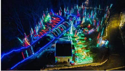 Aerial view of a house surrounded by vibrant, colorful holiday lights and decorations in a wooded area.