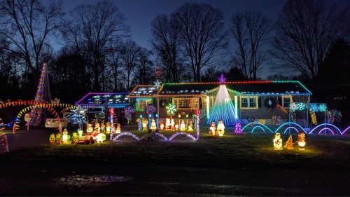 A brightly lit house decorated with colorful Christmas lights and festive lawn decorations, including snowmen and trees.