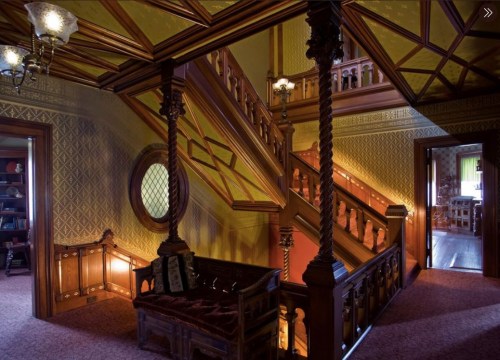 A beautifully ornate staircase in a vintage home, featuring intricate woodwork and warm lighting.