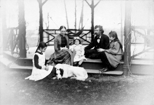A vintage black-and-white photo of a family with two adults, three children, and a dog sitting on a gazebo porch.