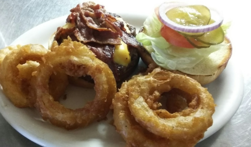 A plate featuring a bacon cheeseburger with lettuce, tomato, and pickles, alongside crispy onion rings.