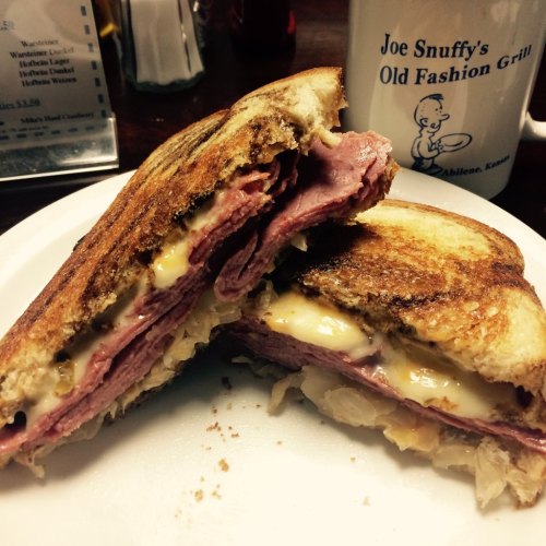 A close-up of a grilled sandwich with layers of ham, melted cheese, and sauerkraut on toasted bread, served on a plate.