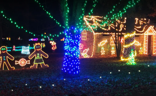 Colorful holiday lights illuminate a festive scene with gingerbread figures and a decorated house among trees.