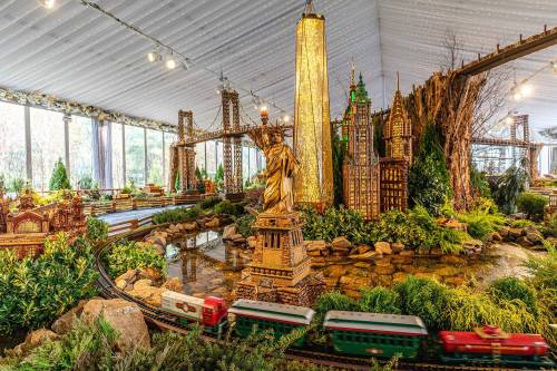 A miniature cityscape featuring iconic landmarks, a train, and lush greenery in a festive indoor setting.