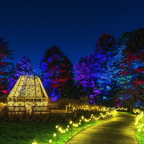 A beautifully lit gazebo surrounded by colorful trees and glowing pathway lights at night.