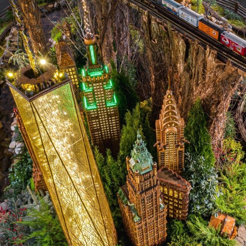 A vibrant display of miniature skyscrapers surrounded by greenery, with a train passing through a scenic landscape.