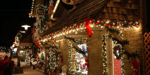 A festive storefront decorated with Christmas lights, wreaths, and ribbons, creating a warm holiday atmosphere at night.
