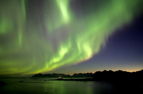 A stunning display of the Northern Lights illuminates the night sky over a tranquil landscape and mountains.