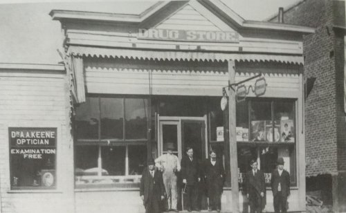 Historic drug store with six men in front, one holding a cane, and a sign for an optician nearby.