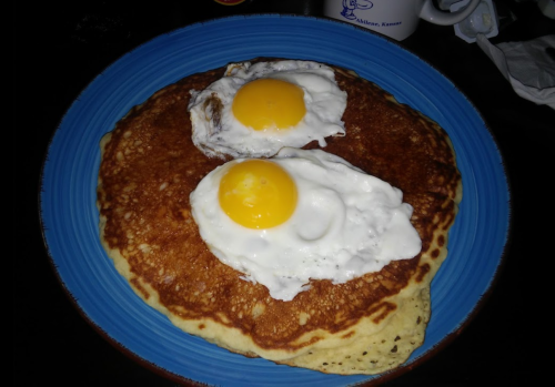 A blue plate with two sunny-side-up eggs on top of a large pancake.