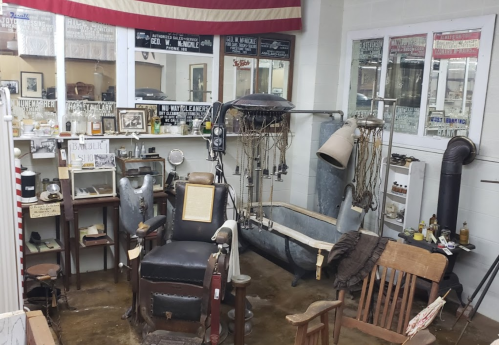 A vintage barber shop setup featuring an old barber chair, tools, and a bathtub in a museum display.