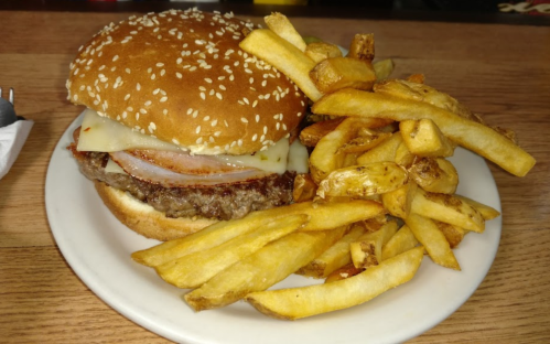 A sesame seed bun burger with cheese and ham, served with a side of golden French fries on a white plate.