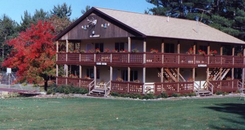 A two-story wooden lodge surrounded by trees, featuring flower boxes and vibrant fall foliage.
