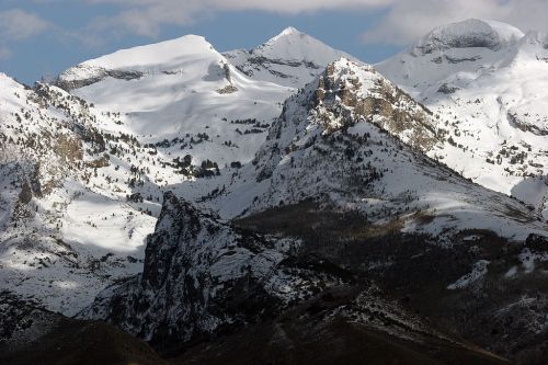 Snow-capped mountains under a cloudy sky, showcasing rugged peaks and a mix of rocky and snowy terrain.