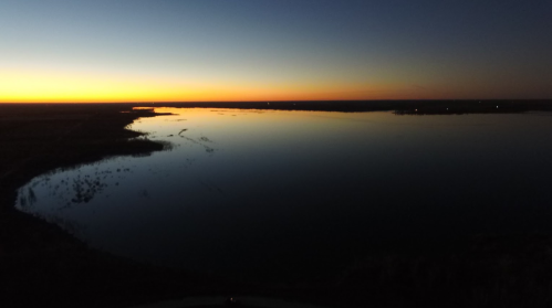 A serene river at sunset, reflecting vibrant orange and blue hues across the calm water.